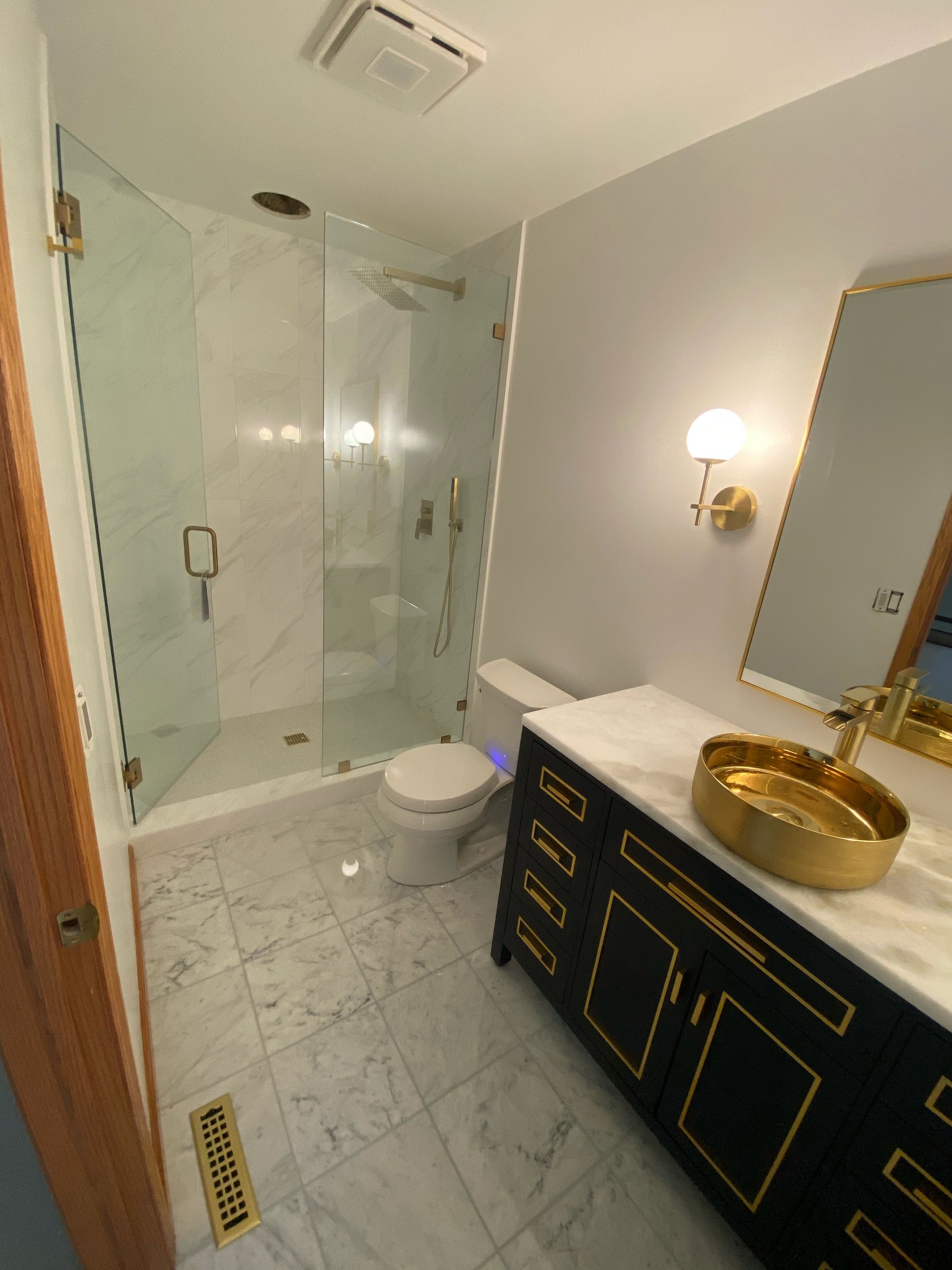 Modern luxury bathroom with marble, brass accents & frameless glass shower